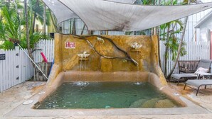 A small outdoor pool with a waterfall feature, surrounded by a white fence and palm trees. - Harbor Walk Hideaways | Group Compound In Old Town, Pool! (Key West)