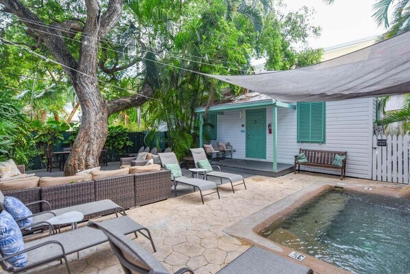 Un patio con mobiliario de mimbre, una piscina pequeña y un edificio con contraventanas verdes.