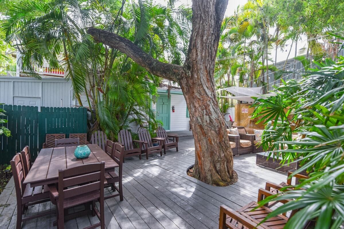 Een houten terras met een tafel en stoelen, omgeven door weelderig groen en een grote boom.