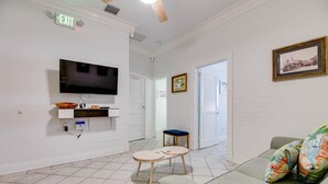 A living room with a flat-screen TV, a small table with a blue cushion, a sofa with colorful cushions, and an exit sign. - Atocha Cottage at Harbor Walk Hideaways | 2 Blocks From Duval! (Key West)