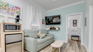 A compact living space with a kitchenette, a grey sofa, a small round table, and a TV mounted on the wall. - Pilar Cottage | Spectacular Studio w/ Shared Pool (Key West)