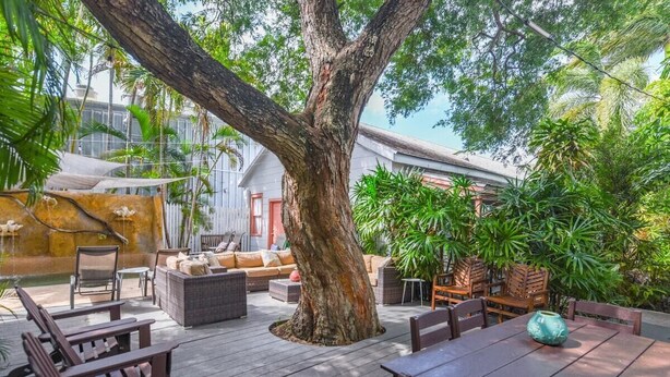 An outdoor patio area with wooden furniture, a large tree, and lush greenery. - Pilar Cottage | Spectacular Studio w/ Shared Pool (Key West)