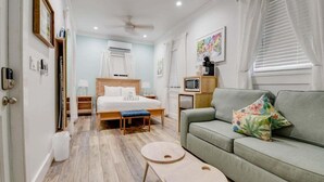 A modern hotel room with a bed, a sofa, a small table, and a TV. - Pilar Cottage | Spectacular Studio w/ Shared Pool (Key West)