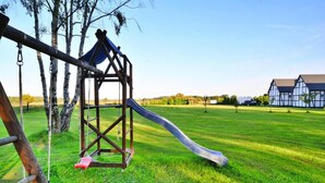 A playground with a slide and swings in a grassy field with a house in the background. - Comfortable Bungalows With a Fireplace and Terrace, Jaroslawiec (Postomino)