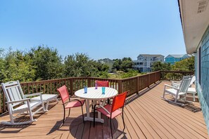 A wooden deck with a round table and chairs, surrounded by a wooden railing. - Classic Outer Banks soundside beach house near Duck Town Park! (Duck)