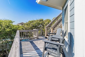 A wooden deck with a railing, a staircase, and two chairs.