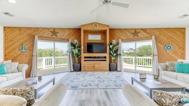 Een ruime woonkamer met een houten wand, een plafondventilator, een flatscreen televisie en een groot raam met uitzicht op een balkon.