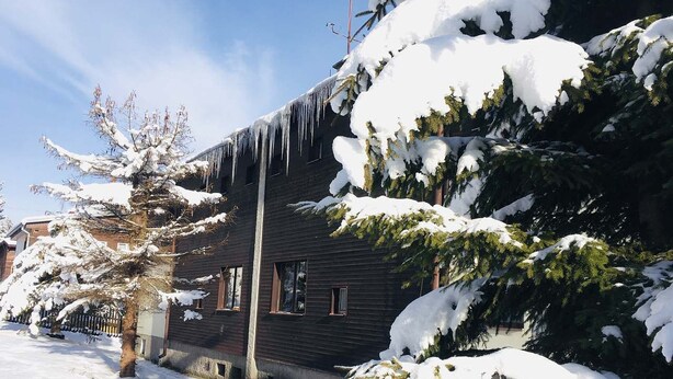 Una casa de madera oscura con árboles cubiertos de nieve y estalactitas colgando del techo.