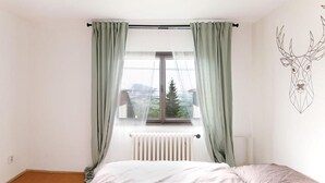 Un dormitorio con cama, ventana con cortinas, radiador y un adhesivo mural de cabeza de ciervo.