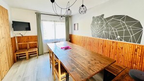 Una habitación con una mesa de madera, bancos, un televisor y una obra de arte geométrica en la pared.