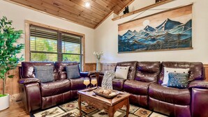 Un salon chaleureux avec un canapé en cuir, une table basse en bois et un tableau représentant des montagnes.