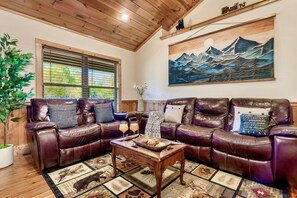 Un salon chaleureux avec un canapé en cuir, une table basse en bois et un tableau représentant des montagnes.