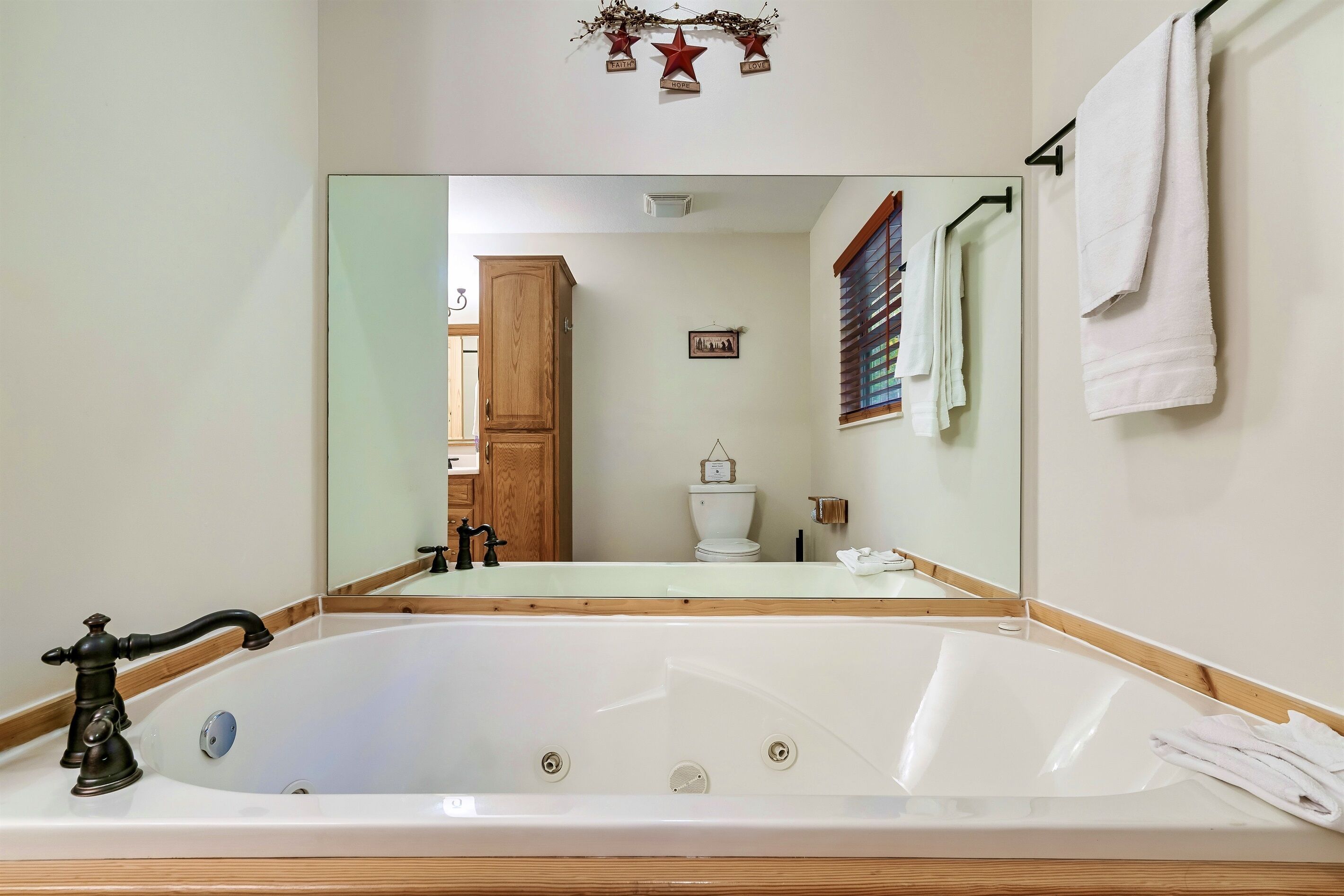 Un baño con una bañera grande, un armario de madera, un inodoro y un espejo.