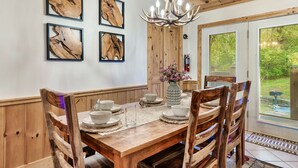 Une table à manger en bois, des chaises assorties, un tableau encadré au mur et un lustre.