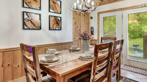 Une table à manger en bois, des chaises assorties, un tableau encadré au mur et un lustre.