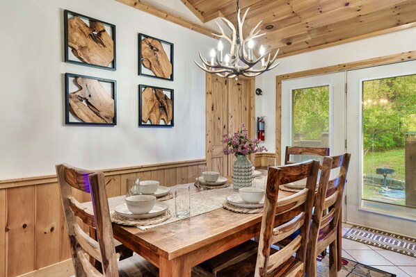 Une table à manger en bois, des chaises assorties, un tableau encadré au mur et un lustre.