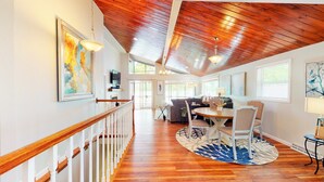 A spacious room with a wooden ceiling, a dining area with a round table and chairs, and a view of the outdoors through large windows.