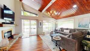 A spacious living room with a wooden ceiling, a fireplace, a television, and a large window overlooking a scenic view.