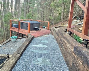 A wooden deck with a hot tub, surrounded by a wooden fence and gravel. - Boho Mtn Vibe'z~ Hot Tub+Fire Pit~ 3 mins to BRP! (Spruce Pine)