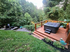 A deck with a hot tub, surrounded by a wooden railing and string lights. - Boho Mtn Vibe'z~ Hot Tub+Fire Pit~ 3 mins to BRP! (Spruce Pine)