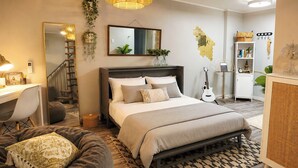 A bedroom with a bed, bedside table, lamp, guitar, and a desk with chair. - “Little Blue Cabin • Cozy Boho Hideaway • Jacuzzi, Fire Pit & Close to BRP” (Spruce Pine)