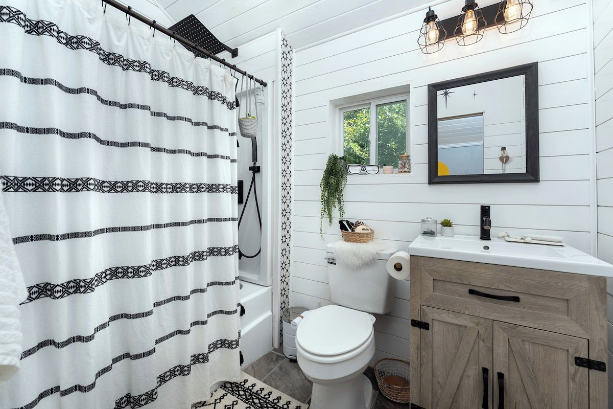 A bathroom with a white shower curtain, a toilet, a sink with a mirror, and a window with plants.