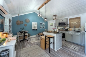 A kitchen with a blue accent wall, wooden flooring, and a bar area with stools. - Boho Mtn Vibe'z~ Hot Tub+Fire Pit~ 3 mins to BRP! (Spruce Pine)