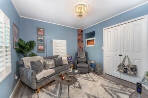 A living room with a grey sofa, a small round coffee table, a patterned rug, a grey armchair, and a white door.