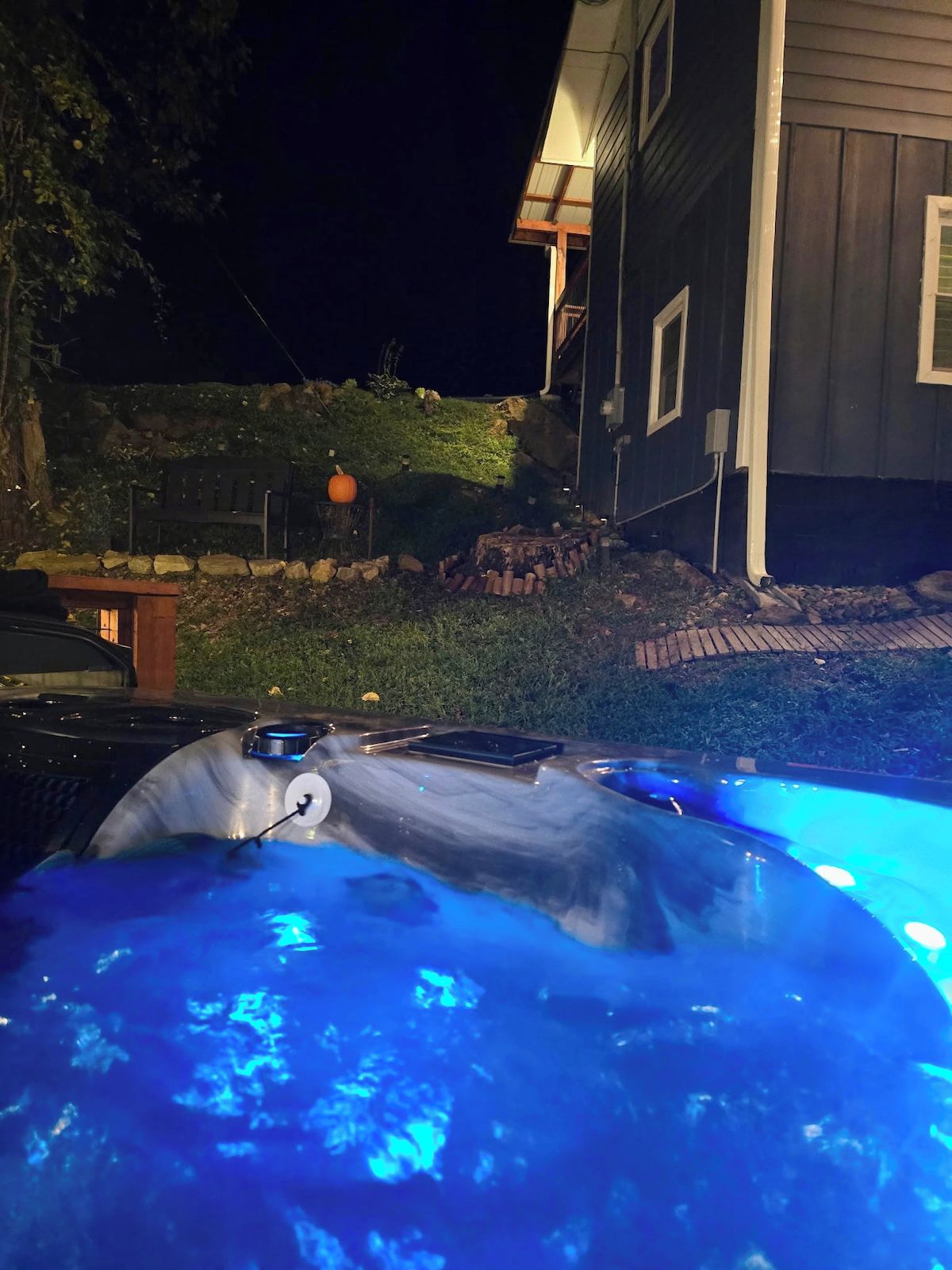 A hot tub with blue lighting, a stone wall, and a house in the background.