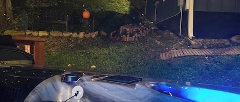A hot tub with blue lighting, a stone wall, and a house in the background.