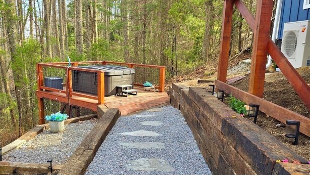 A wooden deck with a barbecue grill, seating area, and a view of a forested area. - “Little Blue Cabin • Cozy Boho Hideaway • Jacuzzi, Fire Pit & Close to BRP” (Spruce Pine)