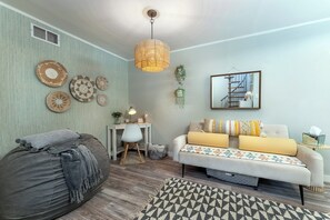 Un salon comprenant un canapé, un fauteuil poire, un tapis à motifs, un luminaire suspendu et des éléments de décoration murale.