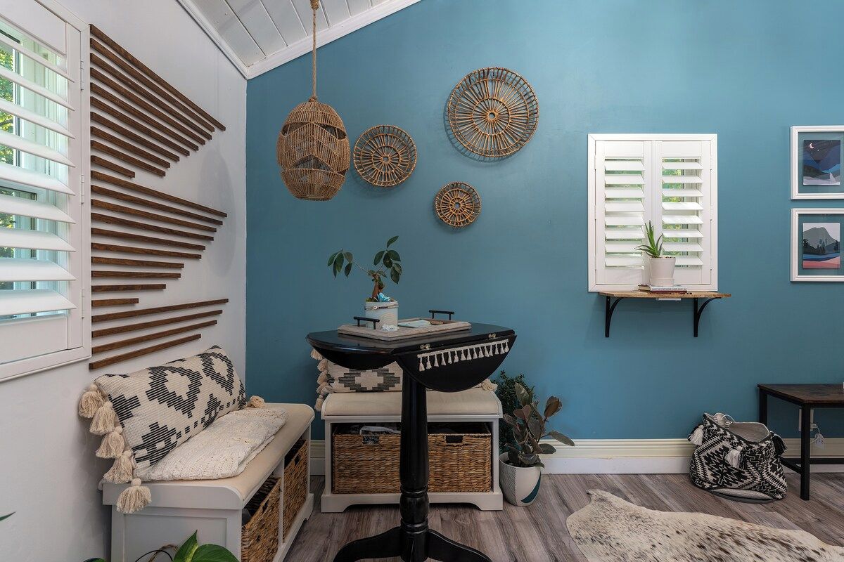 A room with a blue wall, a bench with a patterned throw, a small table with a tray, and decorative wall hangings.