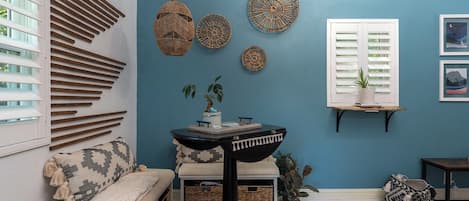 A room with a blue wall, a bench with a patterned throw, a small table with a tray, and decorative wall hangings.