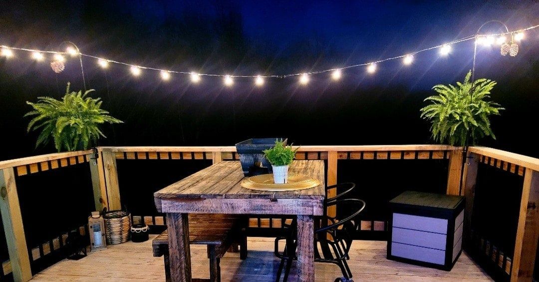 A wooden deck with a table and chairs, string lights, and potted plants.