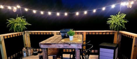 A wooden deck with a table and chairs, string lights, and potted plants.