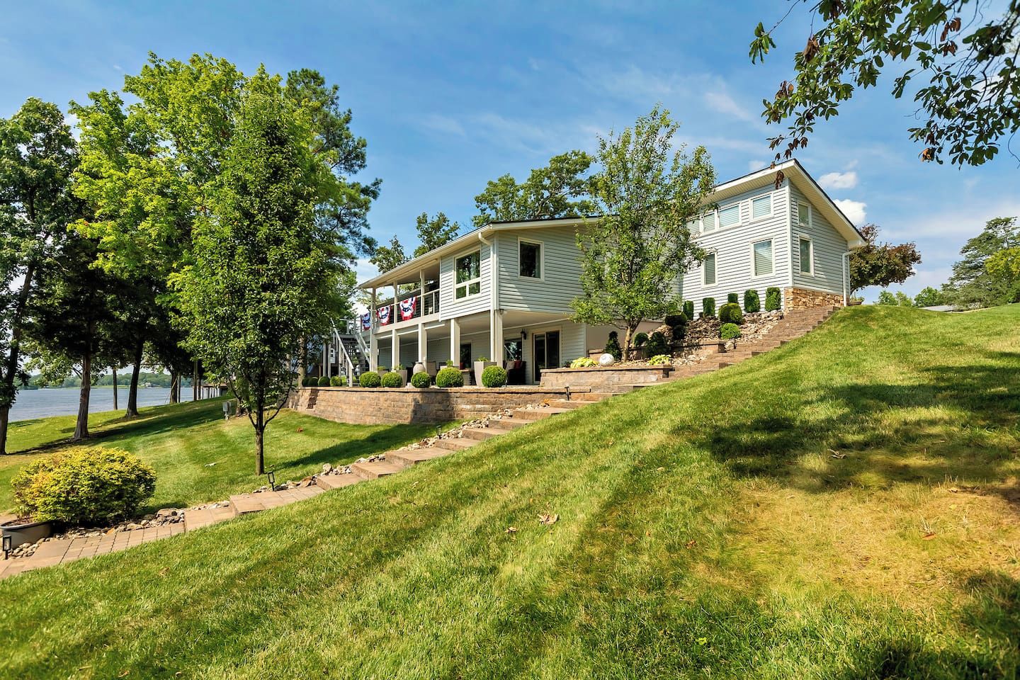A two-story house with a porch, a stone retaining wall, and a grassy hill.