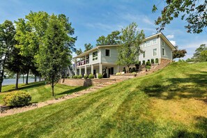 A two-story house with a porch, a stone retaining wall, and a grassy hill.