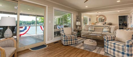 A spacious living room with a large window overlooking a deck, a ceiling fan, and a fireplace.