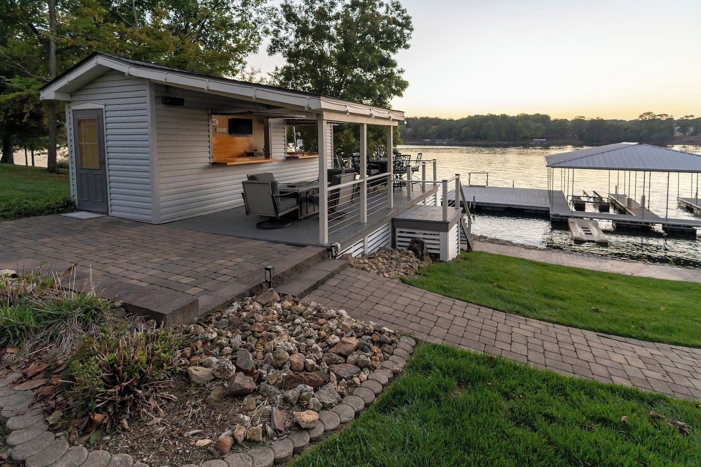 A small cabin with a patio, a dock, and a view of a lake.