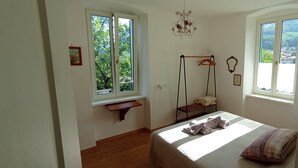 Een slaapkamer met een bed, twee ramen, een hangstoel en een klein plankje.