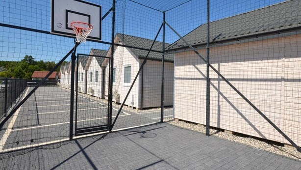 A basketball court with a hoop, surrounded by a wire fence, and adjacent to a building with a tiled roof. - Holiday Home Near Bukowo Lake and Beaches (Darlowo)