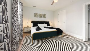 Une chambre à coucher comprenant un lit, un ventilateur de plafond, une table de chevet et une commode, ainsi qu’un tapis à motifs.