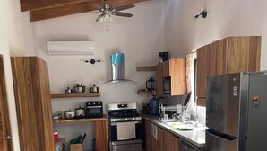 Een keuken met houten kasten, een roestvrijstalen koelkast, een fornuis en een plafondventilator.