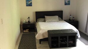 Een slaapkamer met een bed, nachtkastjes, een bankje met schoenenopslag, een plafondventilator en kunstwerken aan de muur.