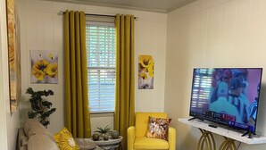 A living room with a grey sofa, yellow cushions, a yellow armchair, a marble coffee table, and a TV on a white stand.