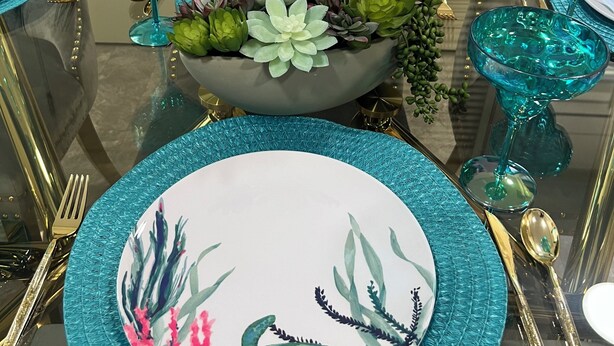A dining table set with teal glassware, gold cutlery, and a centerpiece of succulents.