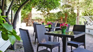 An outdoor seating area with wicker chairs and tables, surrounded by greenery and a stone wall. - Apartment in Pietra Ligure With Garden (Pietra Ligure)