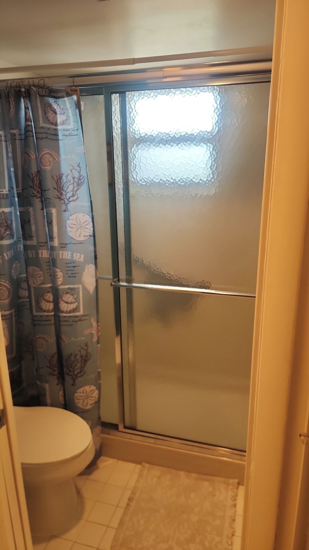 Een badkamer met toilet, douche met glazen deur en een douchegordijn met patroon.