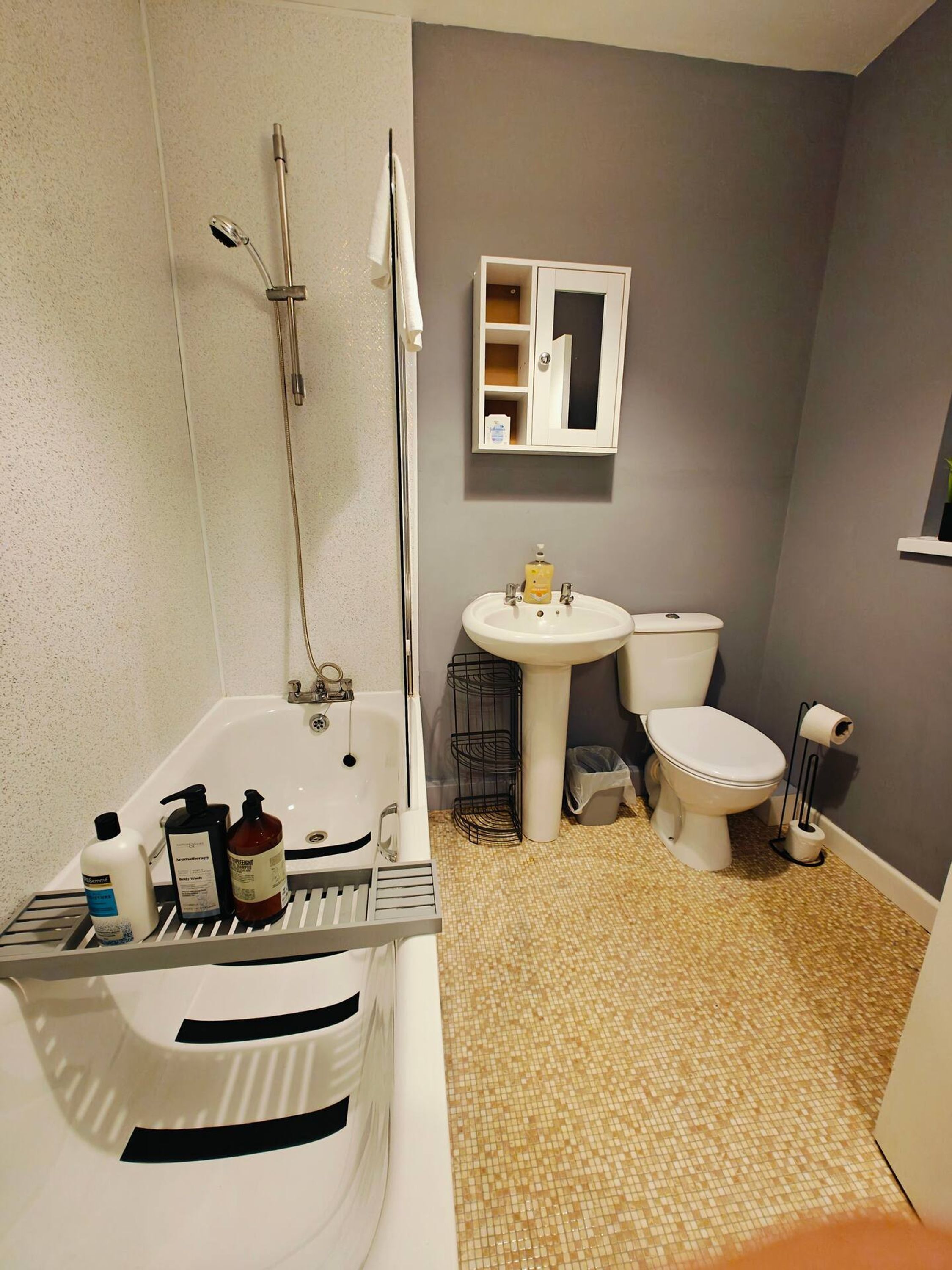 A bathroom with a bathtub, sink, toilet, and a small mirror cabinet.